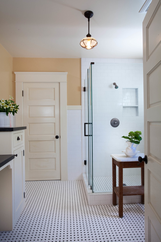 Bild på ett amerikanskt badrum med dusch, med skåp i shakerstil, vita skåp, en hörndusch, vit kakel, tunnelbanekakel, gula väggar, mosaikgolv, ett undermonterad handfat och bänkskiva i täljsten