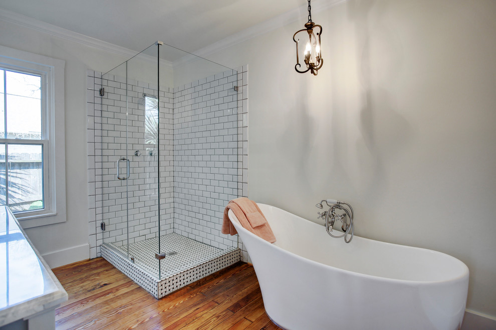 This is an example of a medium sized victorian ensuite bathroom in Houston with beaded cabinets, white cabinets, a freestanding bath, a corner shower, a one-piece toilet, metro tiles, white walls, medium hardwood flooring, a submerged sink, marble worktops, a hinged door and brown floors.