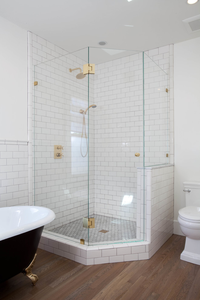 Bild på ett amerikanskt badrum med dusch, med skåp i shakerstil, vita skåp, ett badkar med tassar, en hörndusch, vit kakel, tunnelbanekakel, vita väggar, mellanmörkt trägolv, ett undermonterad handfat och en toalettstol med separat cisternkåpa