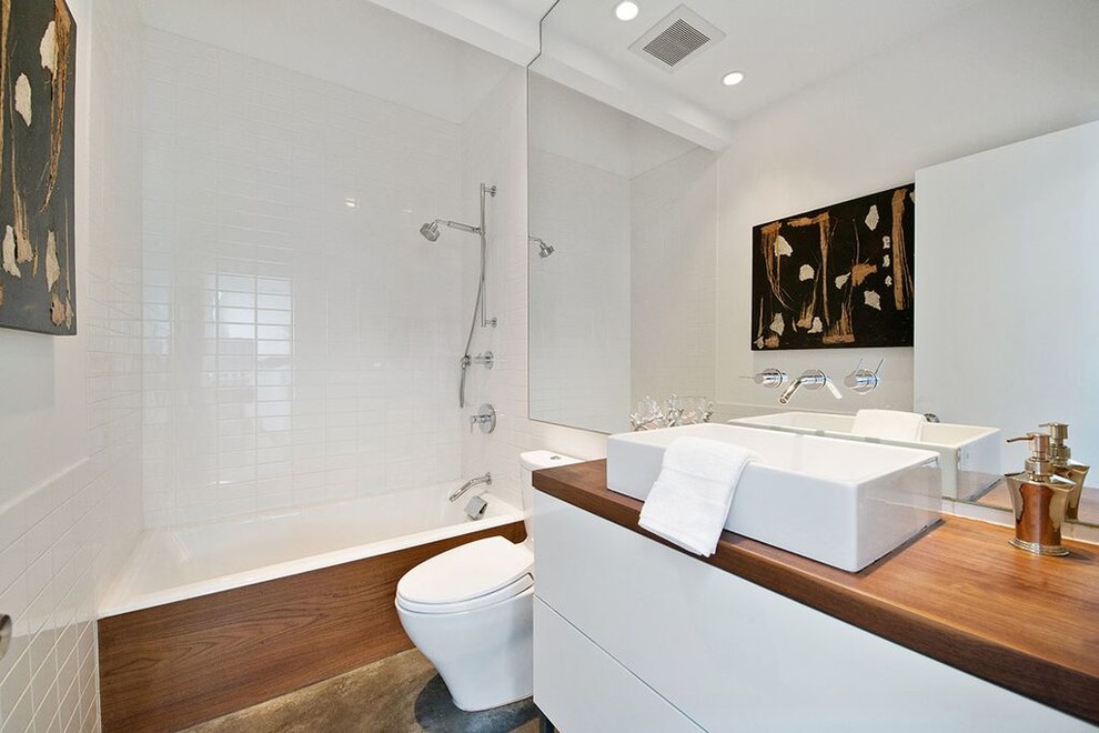Example of a mid-sized minimalist white tile and subway tile concrete floor and brown floor bathroom design in San Francisco with flat-panel cabinets, white cabinets, a two-piece toilet, white walls, a vessel sink and wood countertops