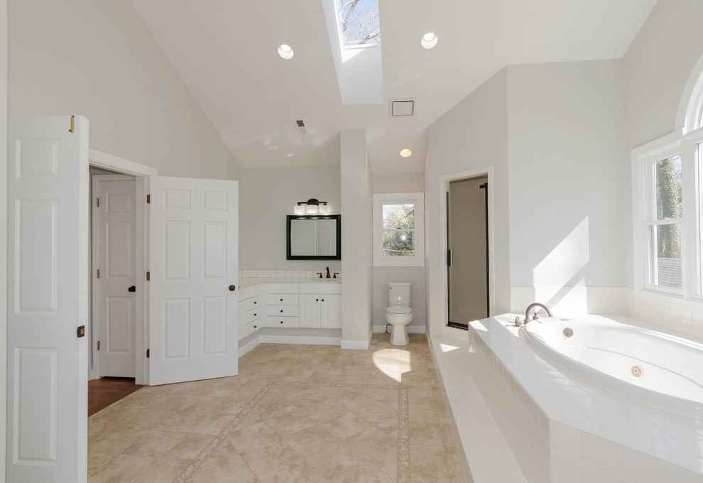 シャーロットにある高級な広いトラディショナルスタイルのおしゃれなマスターバスルーム (インセット扉のキャビネット、白いキャビネット、ドロップイン型浴槽、洗い場付きシャワー、一体型トイレ	、白いタイル、セラミックタイル、白い壁、セラミックタイルの床、一体型シンク、大理石の洗面台、ベージュの床、開き戸のシャワー、白い洗面カウンター) の写真