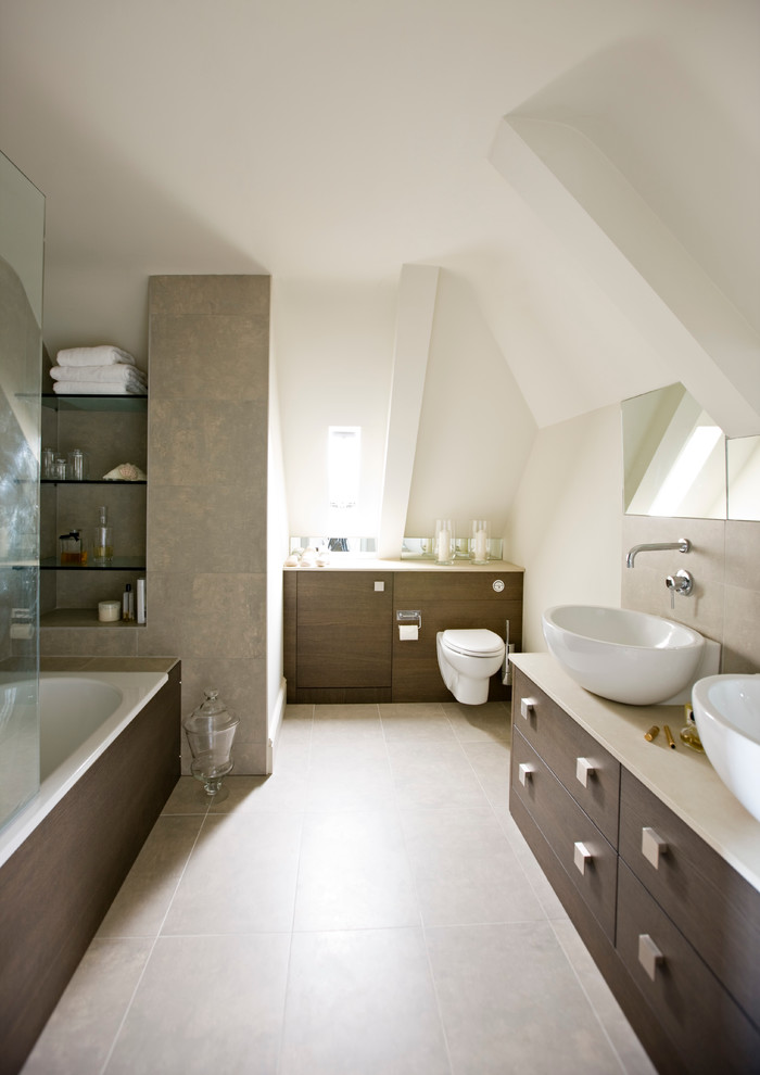 Inspiration for a medium sized contemporary bathroom in London with a vessel sink, flat-panel cabinets, dark wood cabinets, a shower/bath combination, a wall mounted toilet, beige tiles, beige walls, ceramic flooring and a built-in bath.