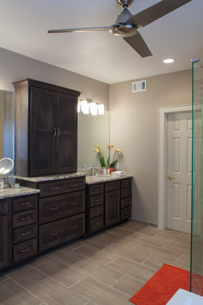 This is an example of a large traditional ensuite bathroom in Kansas City with grey walls, porcelain flooring, beige floors, a corner shower, a submerged sink, a hinged door, recessed-panel cabinets, dark wood cabinets, a freestanding bath and granite worktops.