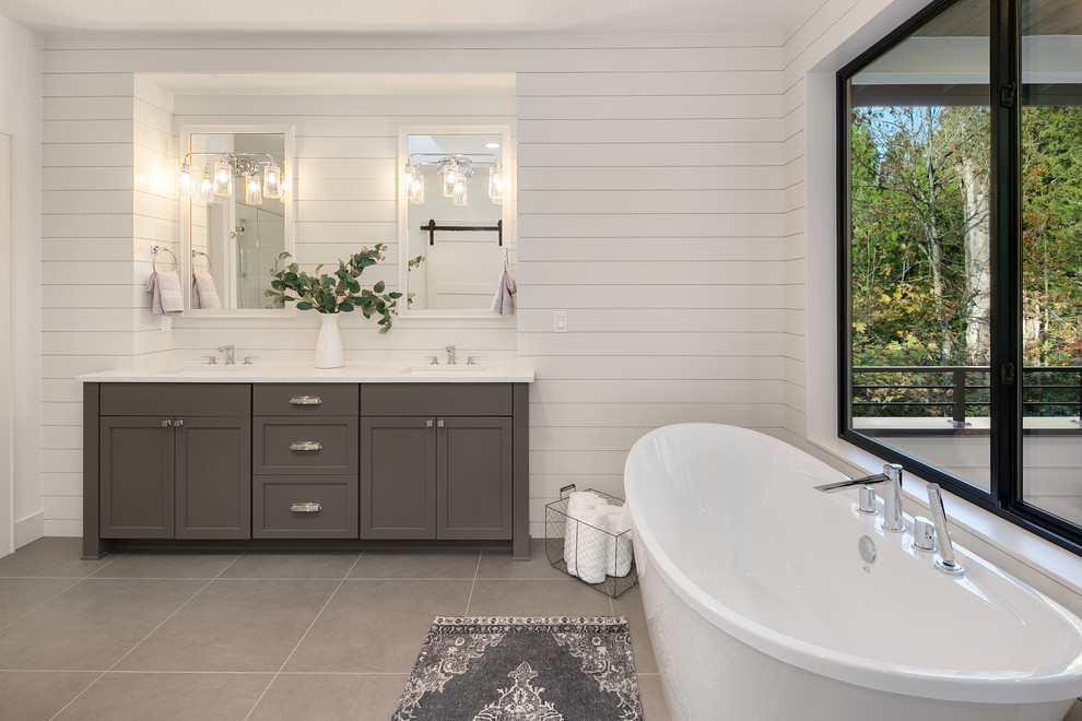 На фото: большая главная ванная комната в стиле кантри с фасадами с утопленной филенкой, серыми фасадами, отдельно стоящей ванной, белыми стенами, врезной раковиной, серым полом и белой столешницей