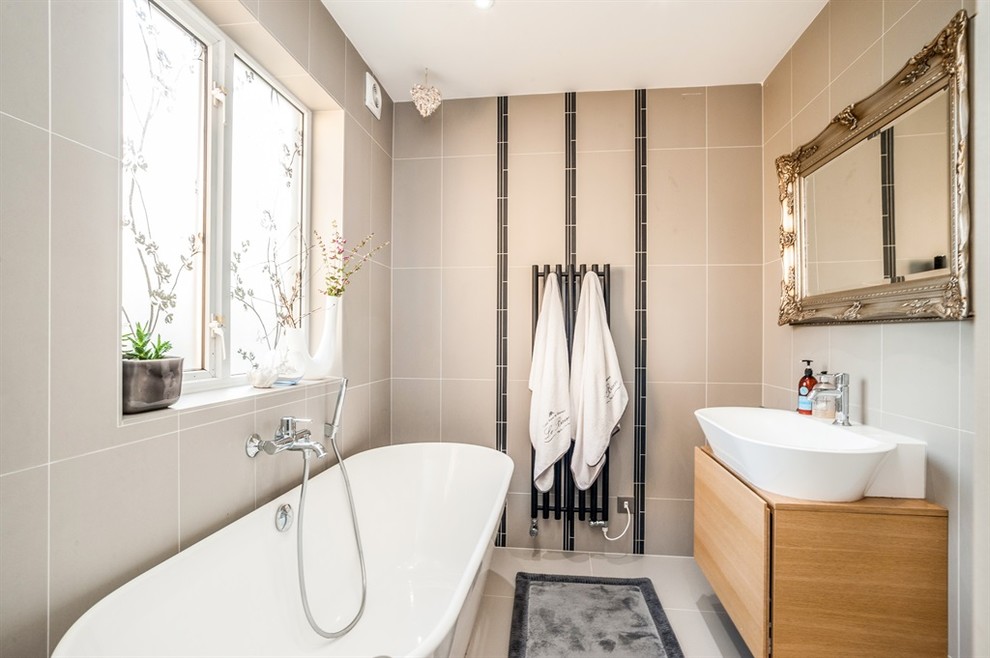 Photo of a medium sized contemporary family bathroom in Hertfordshire with a freestanding bath, a wall mounted toilet, grey tiles, porcelain tiles, grey walls, porcelain flooring, a wall-mounted sink, grey floors, an open shower, flat-panel cabinets and light wood cabinets.