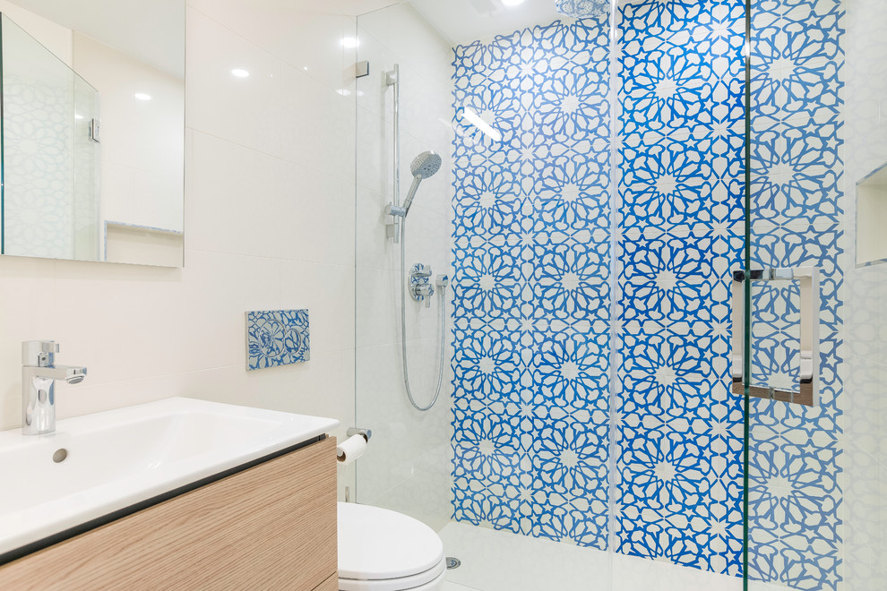 Imagen de cuarto de baño actual de tamaño medio con armarios con paneles lisos, puertas de armario beige, baldosas y/o azulejos azules, baldosas y/o azulejos multicolor, paredes blancas, ducha con puerta con bisagras, baldosas y/o azulejos de cerámica, suelo de madera en tonos medios, aseo y ducha, lavabo de seno grande, encimera de acrílico, suelo marrón, encimeras blancas y ducha empotrada