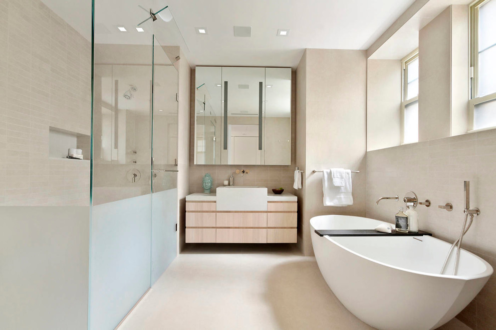 This is an example of a large contemporary ensuite bathroom in New York with light wood cabinets, a freestanding bath, beige tiles, flat-panel cabinets and beige walls.