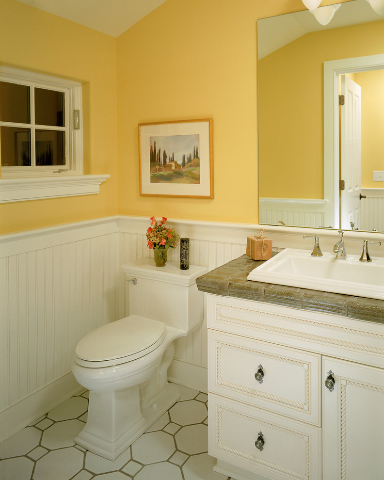 На фото: ванная комната в классическом стиле с накладной раковиной, фасадами с утопленной филенкой, белыми фасадами, столешницей из плитки, унитазом-моноблоком, желтыми стенами и белым полом с