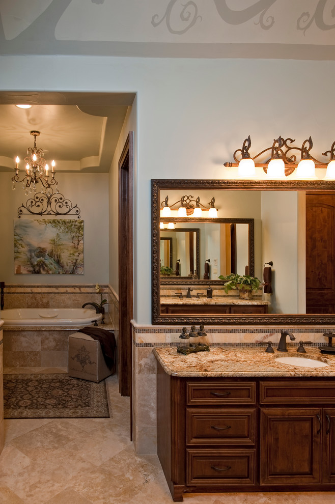 Foto di un'ampia stanza da bagno padronale mediterranea con lavabo da incasso, ante in legno scuro, top in granito, vasca da incasso, piastrelle beige, pareti bianche e pavimento in travertino