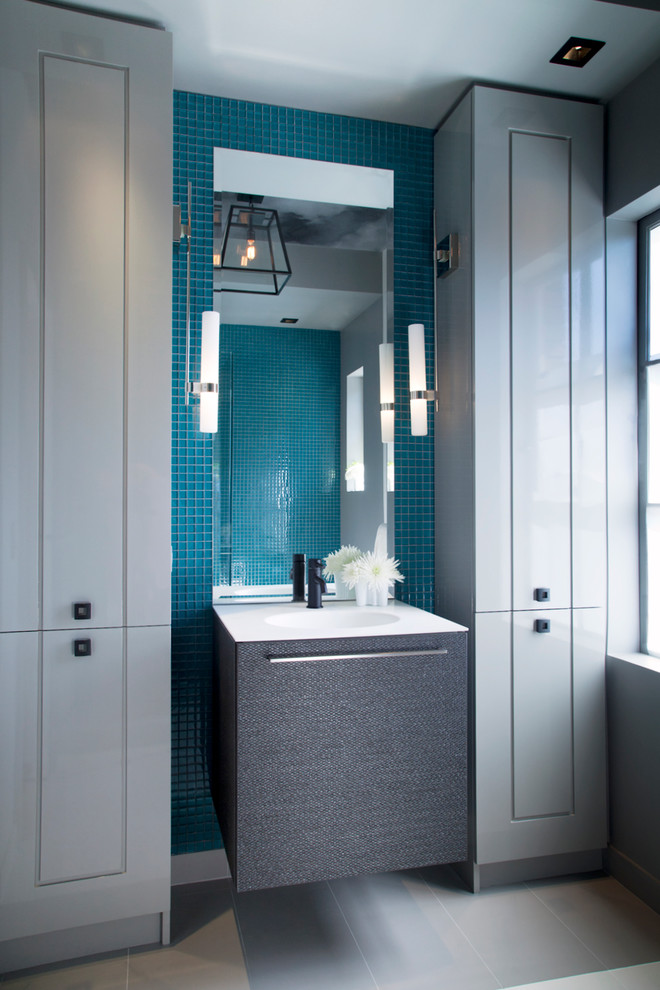 Modern inredning av ett badrum, med grå skåp, blå kakel och mosaik