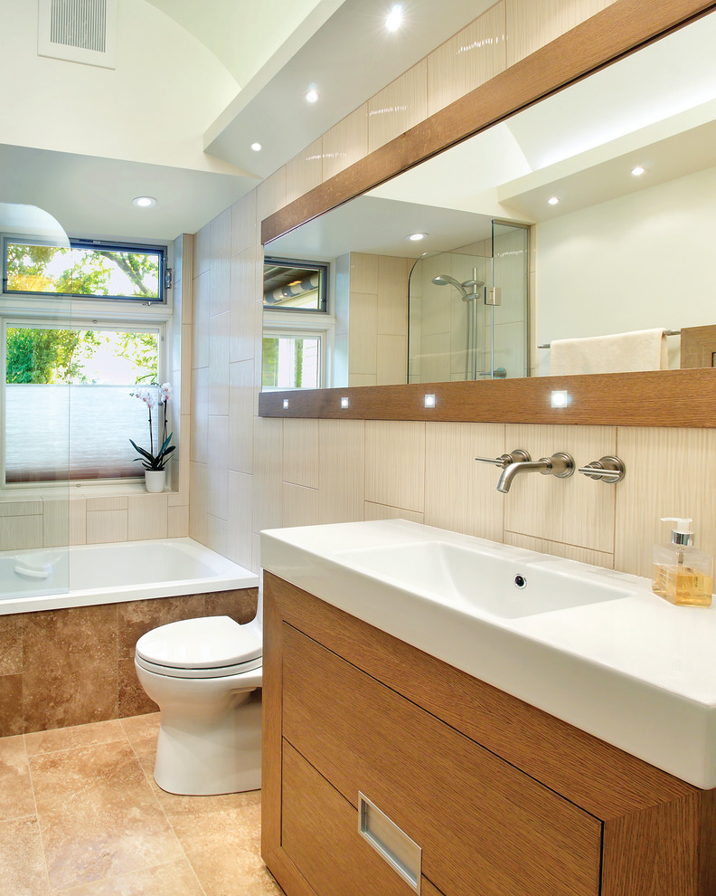 Modernes Badezimmer mit integriertem Waschbecken, flächenbündigen Schrankfronten, hellbraunen Holzschränken, Badewanne in Nische, Duschbadewanne und beigen Fliesen in New York