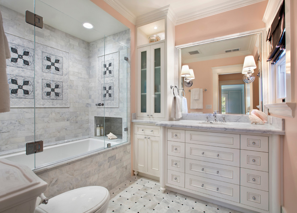 Klassisk inredning av ett badrum, med luckor med infälld panel, vita skåp, ett badkar i en alkov, en dusch/badkar-kombination, vit kakel och rosa väggar