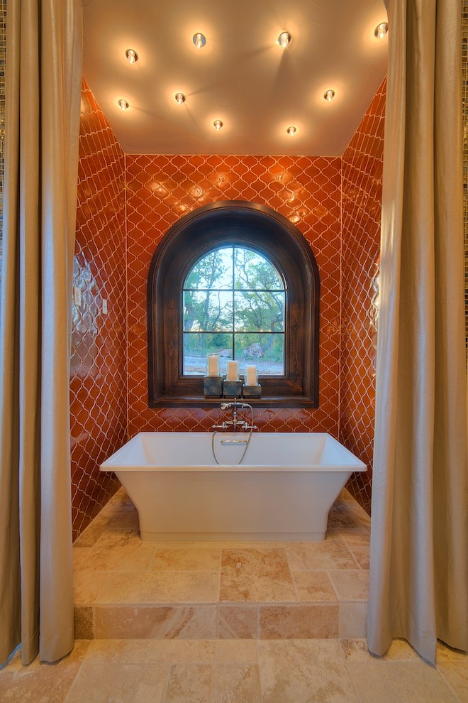 オースティンにある高級な広い地中海スタイルのおしゃれなマスターバスルーム (置き型浴槽、落し込みパネル扉のキャビネット、茶色いキャビネット、オレンジのタイル、セラミックタイル、赤い壁、トラバーチンの床、ベッセル式洗面器、オニキスの洗面台、ベージュの床) の写真