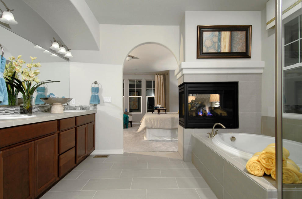 Diseño de cuarto de baño tradicional con lavabo encastrado, puertas de armario de madera en tonos medios, bañera encastrada, baldosas y/o azulejos grises y ventanas