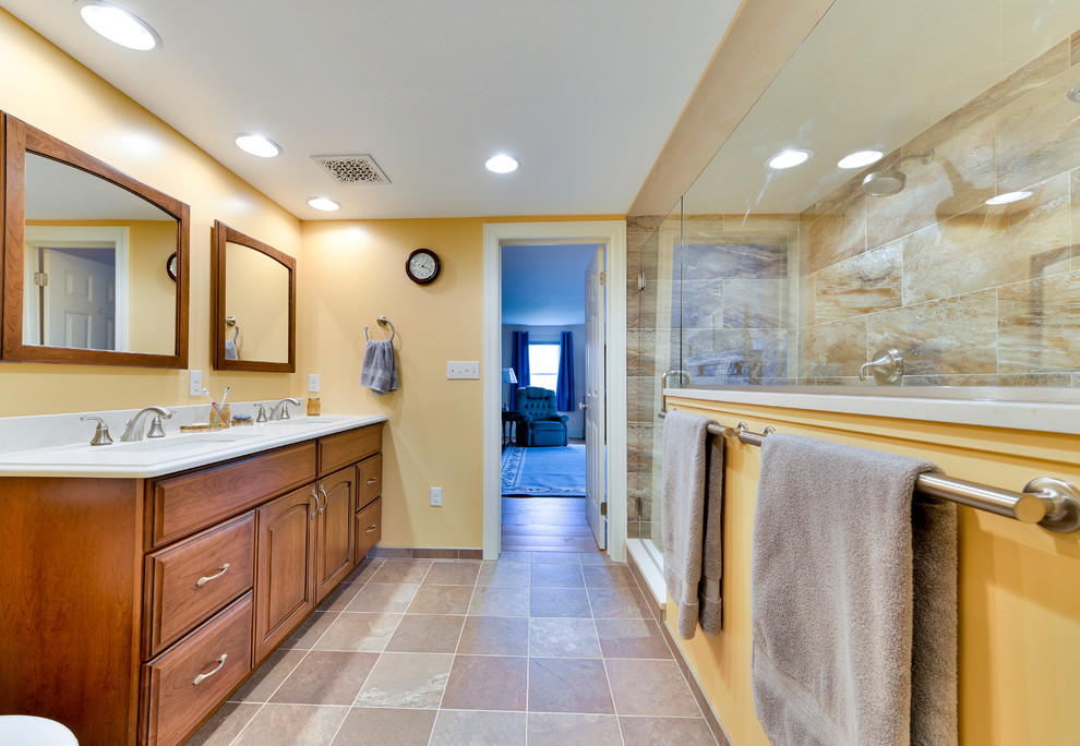Cette photo montre une grande salle de bain nature en bois brun avec un placard avec porte à panneau surélevé, un carrelage beige, des carreaux de porcelaine, un mur jaune, un sol en ardoise, un lavabo encastré, un plan de toilette en quartz modifié, un sol gris et une cabine de douche à porte battante.