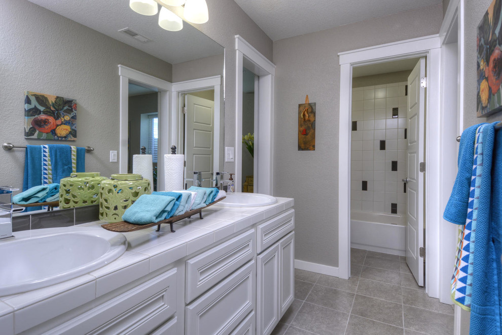 Exempel på ett modernt badrum för barn, med ett nedsänkt handfat, luckor med infälld panel, vita skåp, kaklad bänkskiva, en dusch/badkar-kombination, en toalettstol med hel cisternkåpa, vit kakel, keramikplattor, grå väggar och klinkergolv i keramik