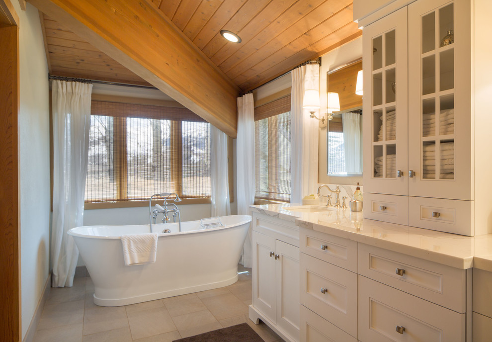 На фото: ванная комната в стиле кантри с врезной раковиной, фасадами с утопленной филенкой, белыми фасадами, отдельно стоящей ванной и белыми стенами
