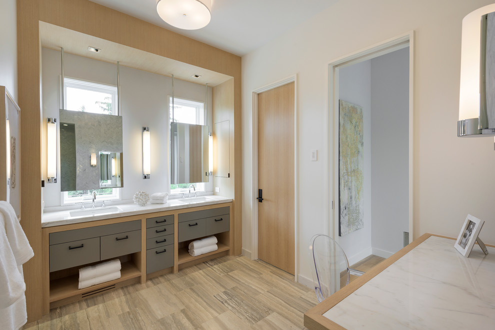 На фото: большая главная ванная комната в современном стиле с врезной раковиной, плоскими фасадами, мраморной столешницей, серой плиткой, каменной плиткой, белыми стенами, полом из травертина, серыми фасадами и зеркалом с подсветкой