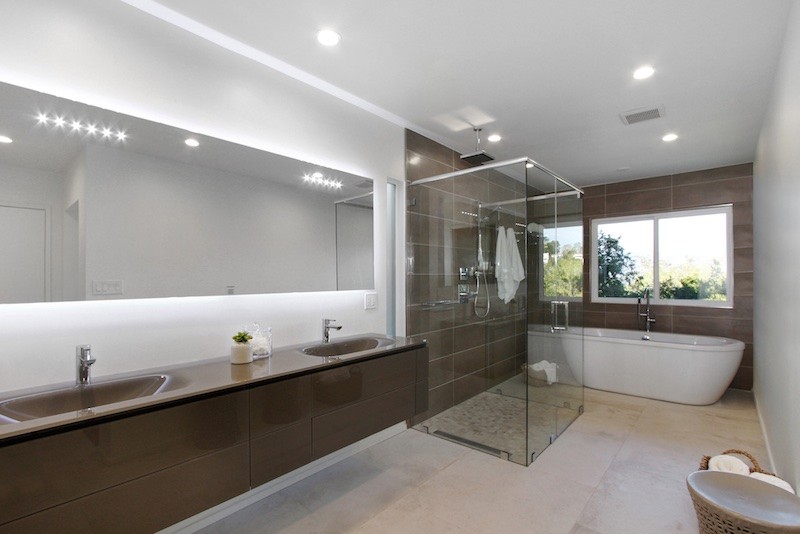 Modern inredning av ett mellanstort en-suite badrum, med ett fristående badkar, vit kakel, porslinskakel, vita väggar, klinkergolv i porslin, bänkskiva i glas, släta luckor, bruna skåp, en kantlös dusch och ett integrerad handfat