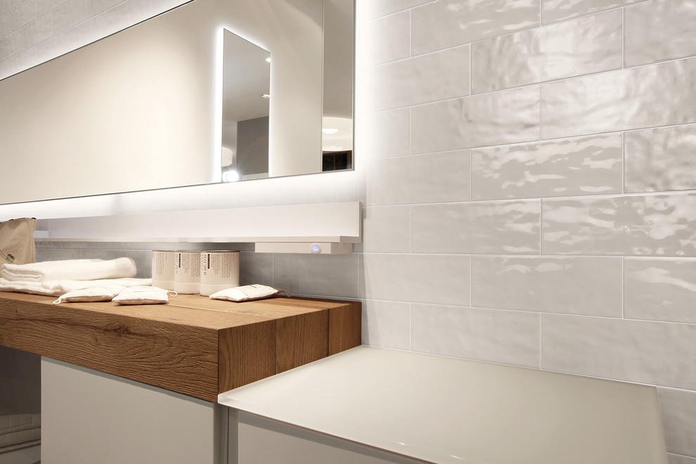 Cette image montre une salle de bain design de taille moyenne avec un placard à porte plane, des portes de placard blanches, un carrelage blanc, un carrelage en pâte de verre, un mur blanc et un plan de toilette en surface solide.