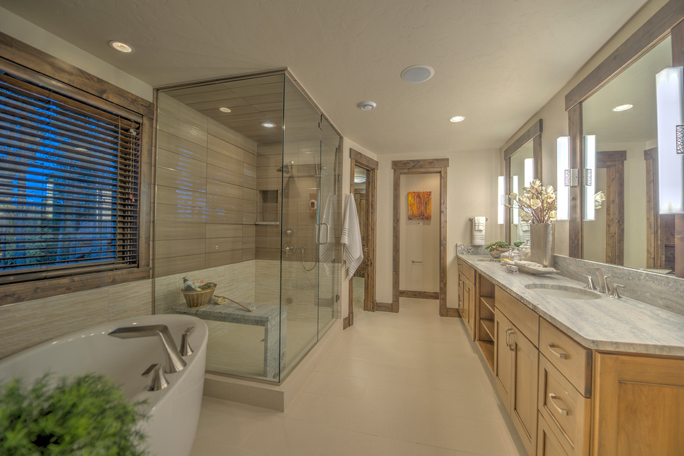 Cette photo montre une grande salle de bain chic en bois clair avec un placard avec porte à panneau encastré, une baignoire indépendante, un carrelage beige, un mur beige, un lavabo encastré et un plan de toilette en granite.