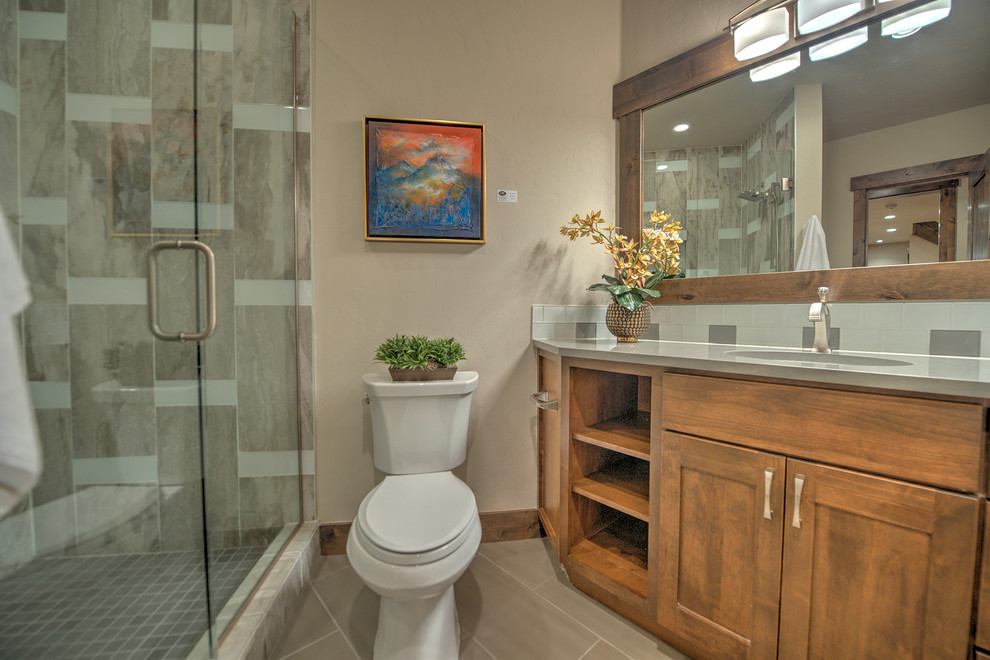 Klassisk inredning av ett mellanstort badrum med dusch, med luckor med infälld panel, skåp i mellenmörkt trä, en toalettstol med separat cisternkåpa, grå kakel, keramikplattor, beige väggar, klinkergolv i keramik, ett undermonterad handfat och bänkskiva i kvarts