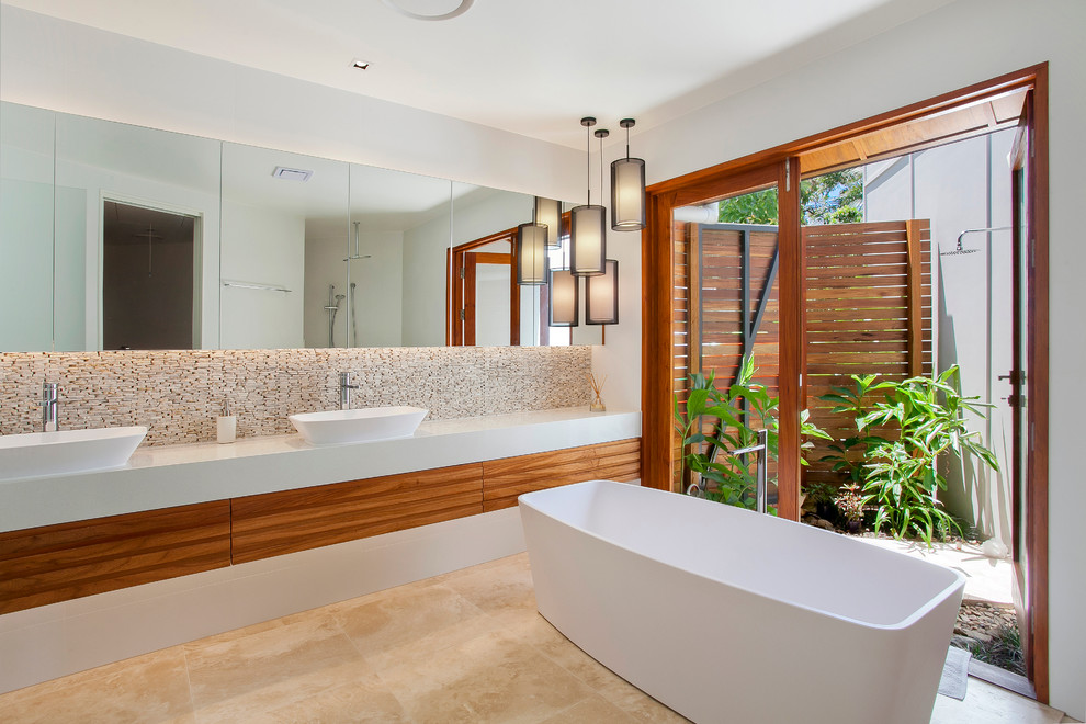 Inredning av ett modernt badrum, med släta luckor, skåp i mellenmörkt trä, ett fristående badkar, en öppen dusch, beige kakel, vita väggar och ett fristående handfat