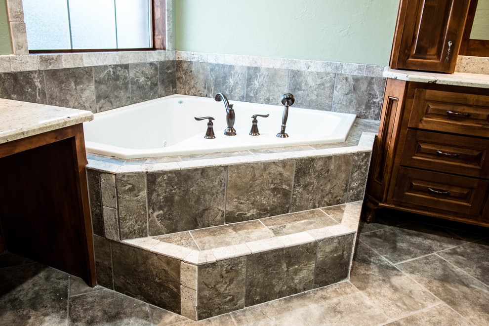 Example of a large mountain style master beige tile and stone tile travertine floor corner bathtub design in Oklahoma City with raised-panel cabinets, dark wood cabinets, blue walls, an undermount sink and granite countertops