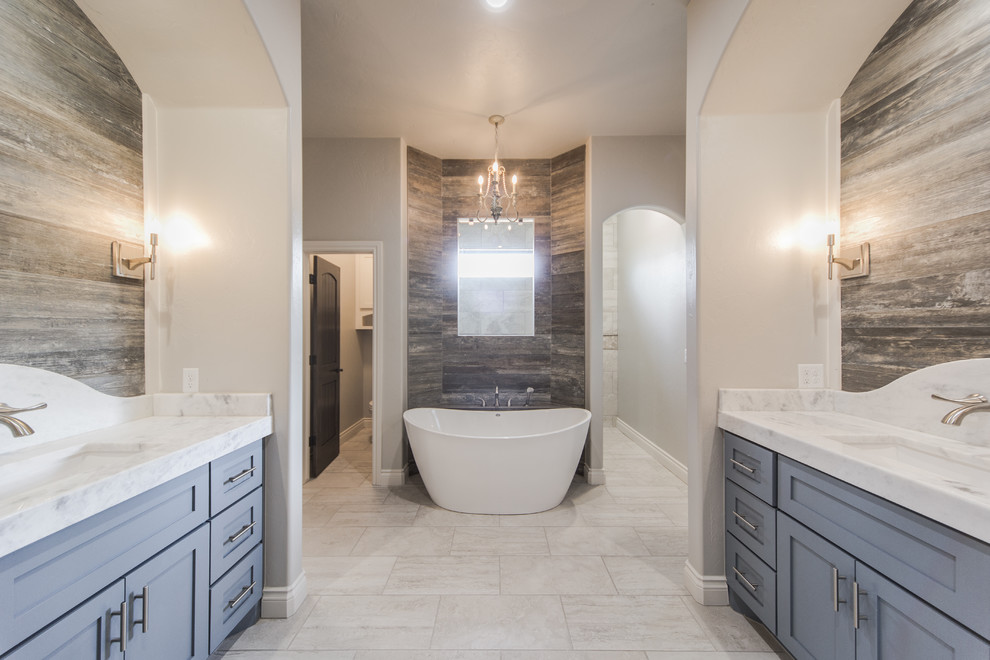 Design ideas for a large traditional ensuite bathroom in Oklahoma City with shaker cabinets, grey cabinets, a freestanding bath, a shower/bath combination, a two-piece toilet, beige tiles, stone tiles, grey walls, porcelain flooring, a submerged sink and marble worktops.