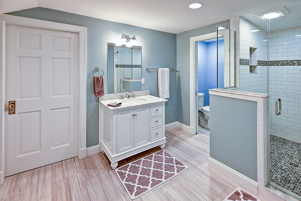 Cette photo montre une grande salle de bain bord de mer pour enfant avec un placard à porte shaker, des portes de placard blanches, une douche d'angle, WC séparés, un carrelage beige, des carreaux de porcelaine, un mur bleu, un sol en carrelage de porcelaine et un lavabo posé.