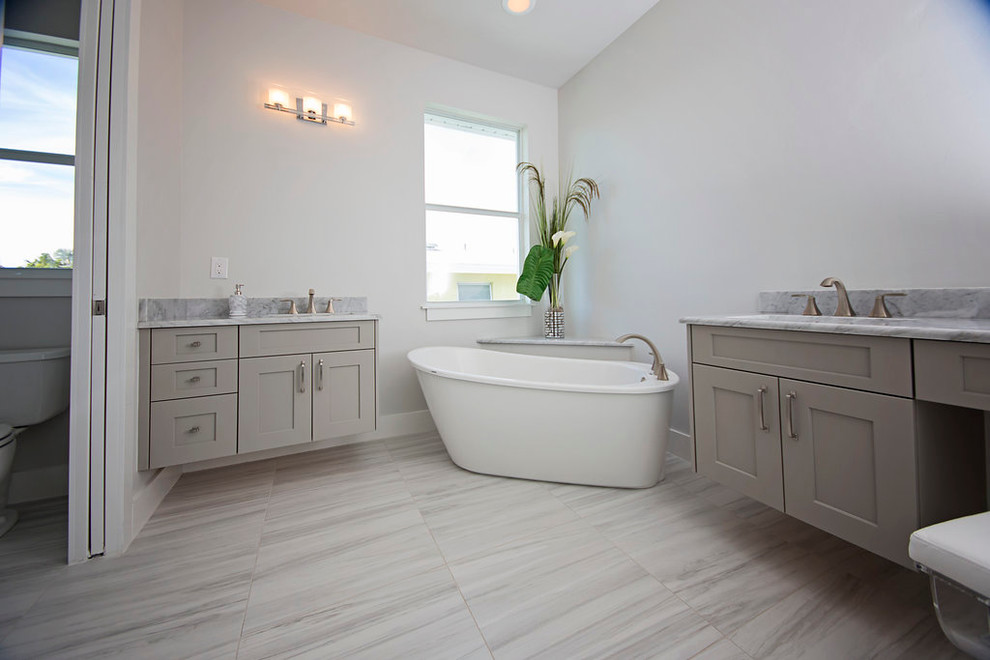 Идея дизайна: большая главная ванная комната в стиле модернизм с фасадами с утопленной филенкой, серыми фасадами, отдельно стоящей ванной, раздельным унитазом, серой плиткой, белой плиткой, каменной плиткой, белыми стенами, мраморным полом, врезной раковиной и мраморной столешницей