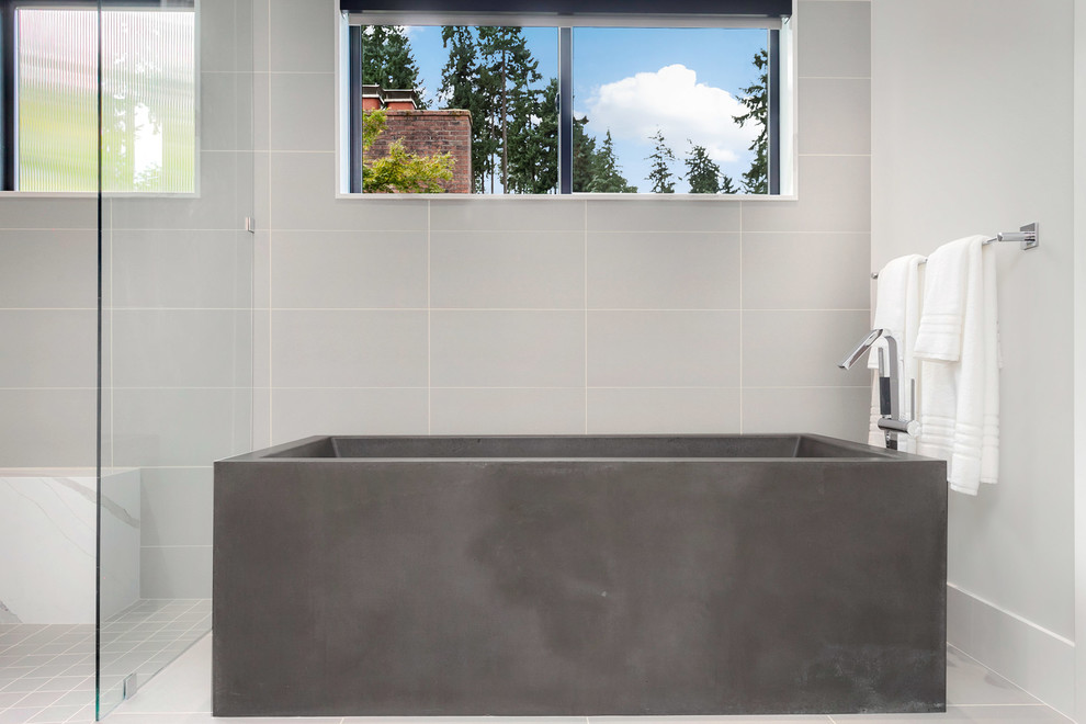 Cette image montre une grande salle de bain principale design avec un placard à porte plane, des portes de placard grises, une baignoire indépendante, un carrelage gris, un mur gris, un lavabo encastré, un plan de toilette en quartz modifié et un sol gris.