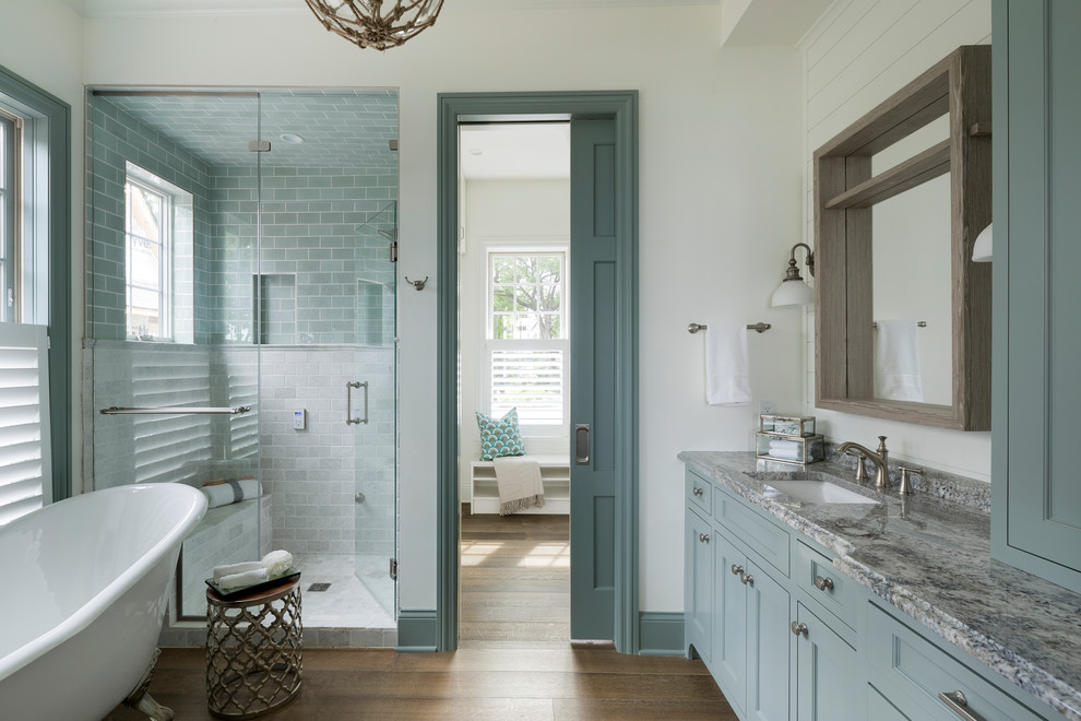 Photo of a nautical ensuite bathroom in Minneapolis with recessed-panel cabinets, turquoise cabinets, a claw-foot bath, an alcove shower, white walls, medium hardwood flooring, a submerged sink, brown floors and a hinged door.