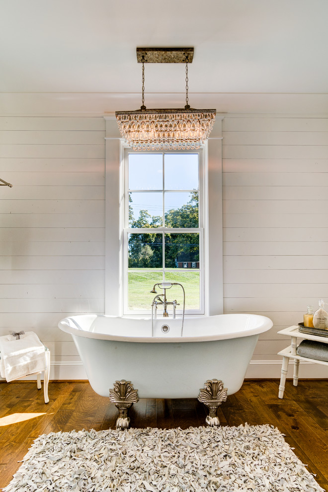 Immagine di una grande stanza da bagno country con vasca con piedi a zampa di leone, pareti bianche, pavimento in legno massello medio e pavimento marrone