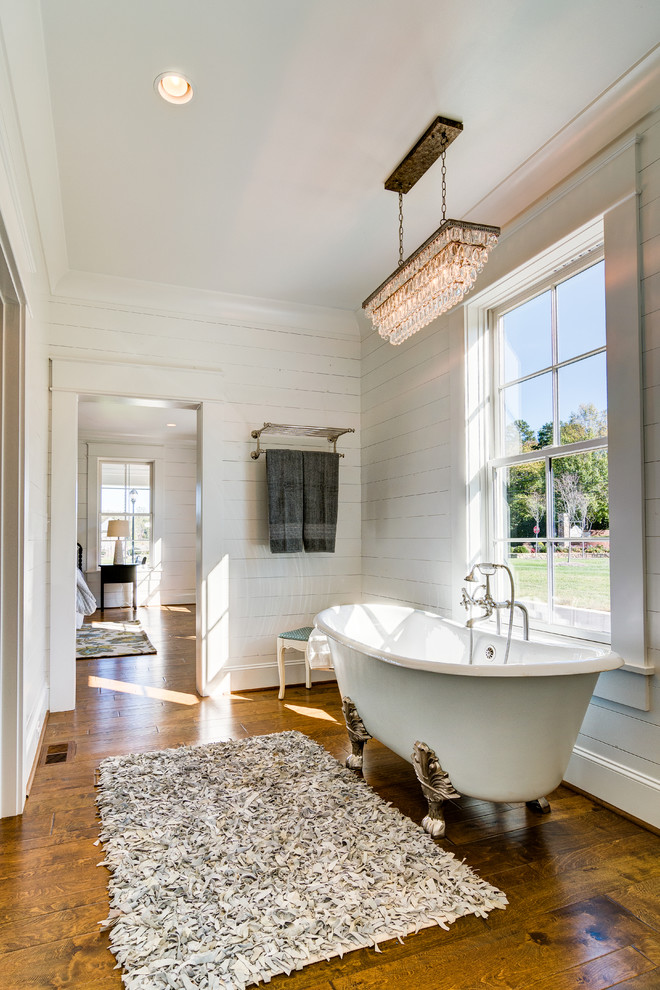 Bild på ett stort lantligt en-suite badrum, med ett badkar med tassar, en öppen dusch, en toalettstol med hel cisternkåpa, vit kakel, vita väggar, mellanmörkt trägolv, ett konsol handfat, marmorbänkskiva, brunt golv och med dusch som är öppen