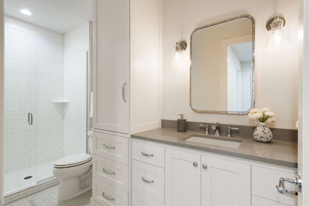 Photo of a medium sized traditional shower room bathroom in Minneapolis with shaker cabinets, white cabinets, white tiles, white walls, engineered stone worktops, grey worktops, an alcove shower, a two-piece toilet, ceramic tiles, mosaic tile flooring, a submerged sink, white floors and a hinged door.