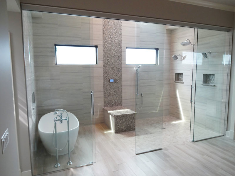 Foto på ett stort funkis en-suite badrum, med ett fristående badkar, en dubbeldusch, grå kakel, porslinskakel, grå väggar, ljust trägolv, grått golv och dusch med skjutdörr