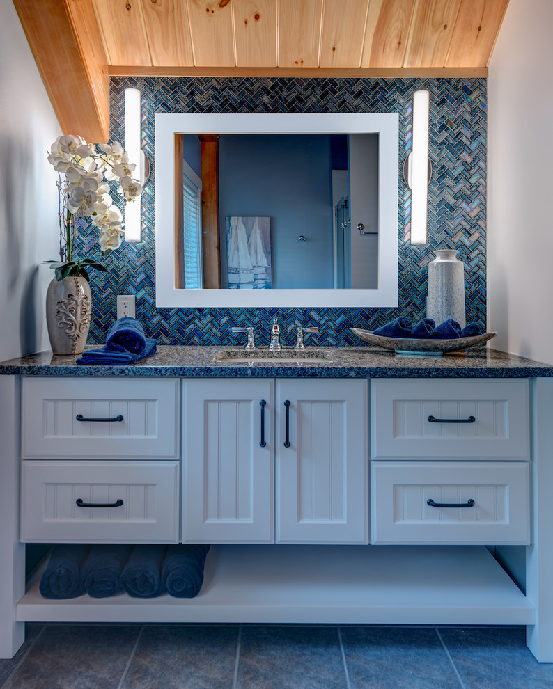 Bild på ett mellanstort amerikanskt badrum med dusch, med luckor med profilerade fronter, vita skåp, en dusch i en alkov, en toalettstol med separat cisternkåpa, blå kakel, glaskakel, grå väggar, klinkergolv i keramik, ett undermonterad handfat, granitbänkskiva, grått golv och dusch med skjutdörr