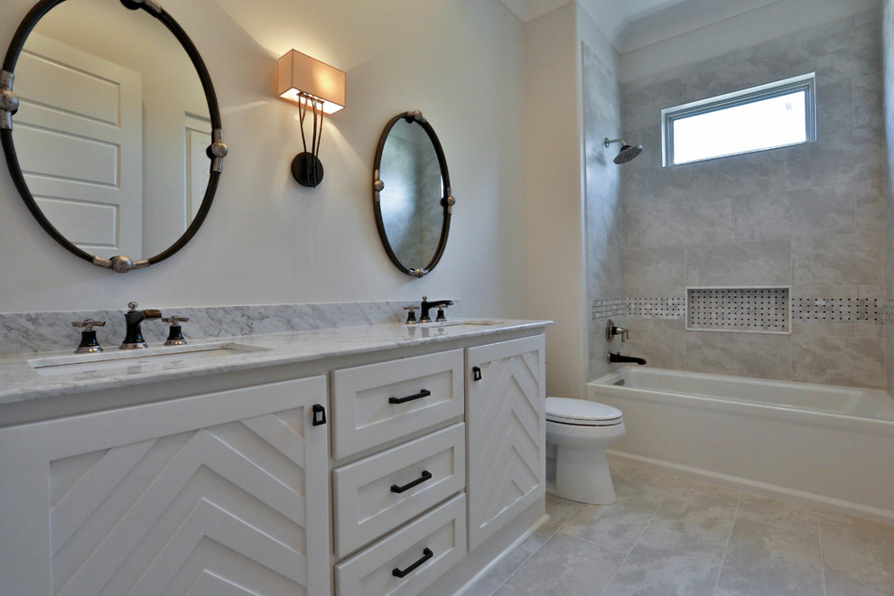 Inredning av ett klassiskt badrum, med skåp i shakerstil, vita skåp, ett badkar i en alkov, en dusch/badkar-kombination, grå kakel, porslinskakel, grå väggar, klinkergolv i porslin, ett undermonterad handfat, marmorbänkskiva, grått golv och med dusch som är öppen