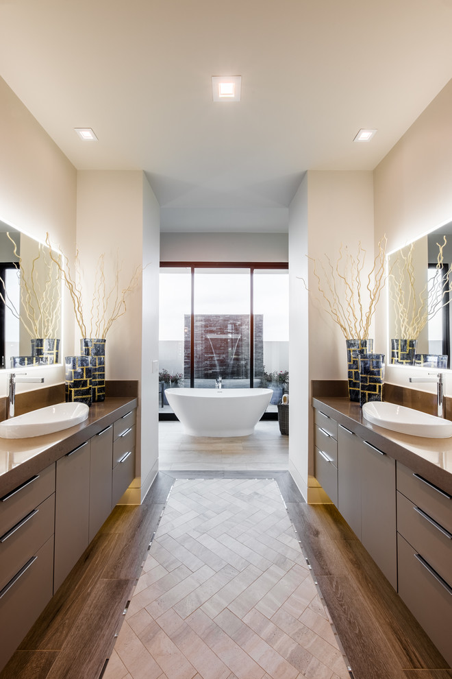 Стильный дизайн: огромная главная ванная комната в стиле модернизм с плоскими фасадами, темными деревянными фасадами, отдельно стоящей ванной, бежевыми стенами, темным паркетным полом, накладной раковиной, столешницей из искусственного камня и разноцветным полом - последний тренд