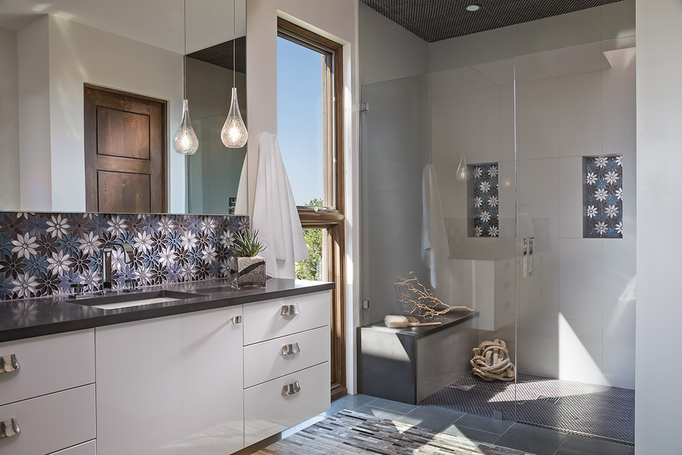 На фото: ванная комната среднего размера в современном стиле с плоскими фасадами, белыми фасадами, душем без бортиков, унитазом-моноблоком, серой плиткой, керамогранитной плиткой, белыми стенами, полом из керамогранита, душевой кабиной, врезной раковиной, столешницей из искусственного камня, серым полом и душем с распашными дверями с