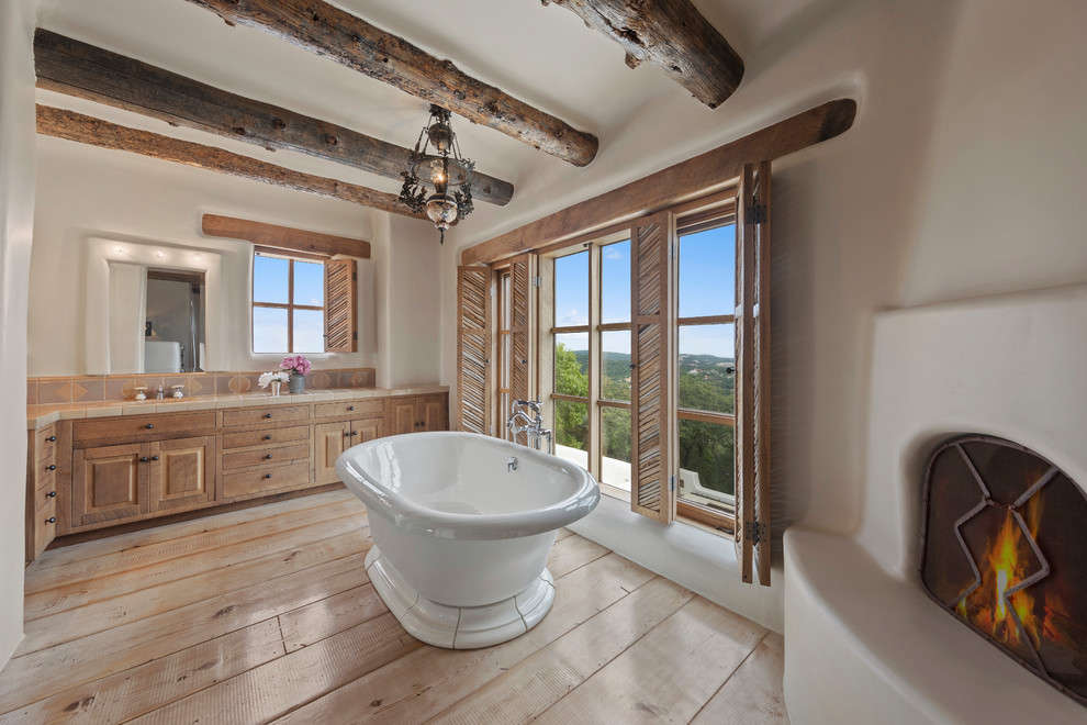 Idée de décoration pour une salle de bain principale sud-ouest américain en bois brun avec un placard avec porte à panneau surélevé, une baignoire indépendante, un mur blanc, parquet clair et un sol beige.