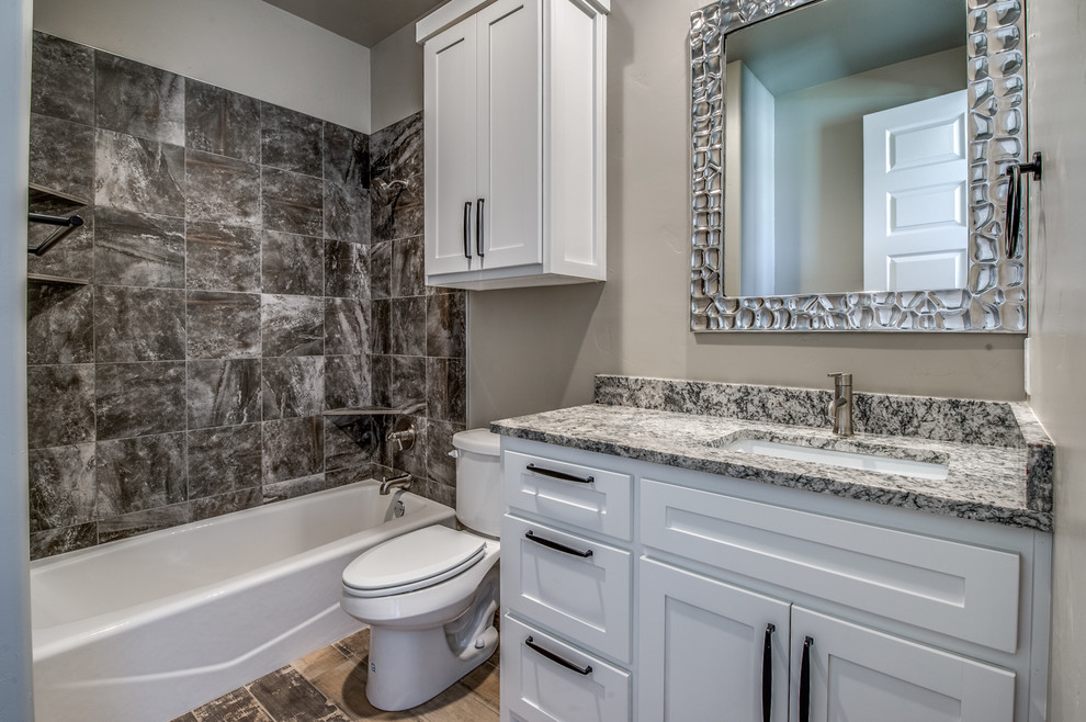 Exempel på ett mellanstort klassiskt en-suite badrum, med skåp i shakerstil, vita skåp, ett badkar i en alkov, en dusch/badkar-kombination, en toalettstol med separat cisternkåpa, grå kakel, porslinskakel, grå väggar, klinkergolv i porslin, ett undermonterad handfat, granitbänkskiva, beiget golv och dusch med duschdraperi