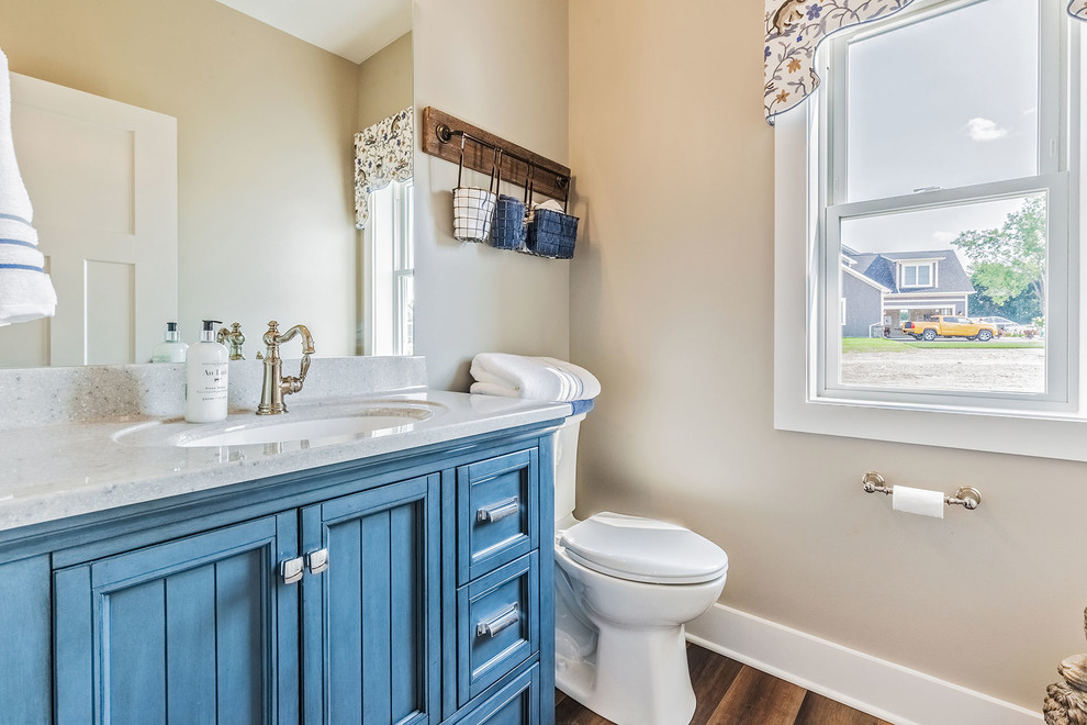 Small 3/4 medium tone wood floor and brown floor bathroom photo in New York with furniture-like cabinets, blue cabinets, a one-piece toilet, beige walls, an undermount sink, quartz countertops and gray countertops