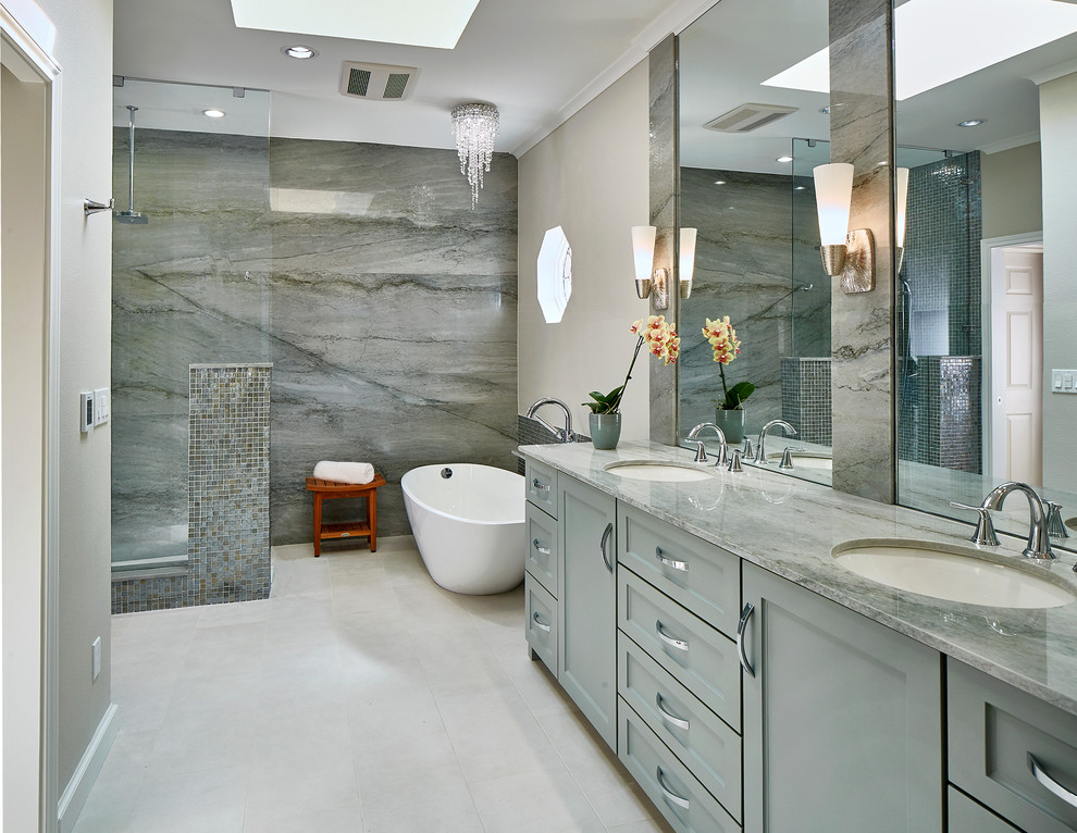 Modelo de cuarto de baño principal clásico renovado con armarios estilo shaker, puertas de armario grises, bañera exenta, ducha esquinera, baldosas y/o azulejos grises, paredes grises, suelo blanco y encimeras grises
