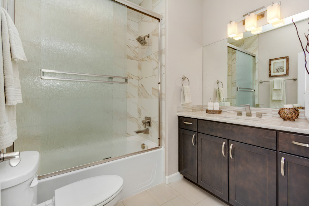 Inspiration för mellanstora amerikanska grått badrum, med luckor med infälld panel, bruna skåp, ett badkar i en alkov, en dusch/badkar-kombination, en toalettstol med separat cisternkåpa, grå kakel, marmorkakel, grå väggar, klinkergolv i porslin, ett undermonterad handfat, marmorbänkskiva, brunt golv och dusch med skjutdörr