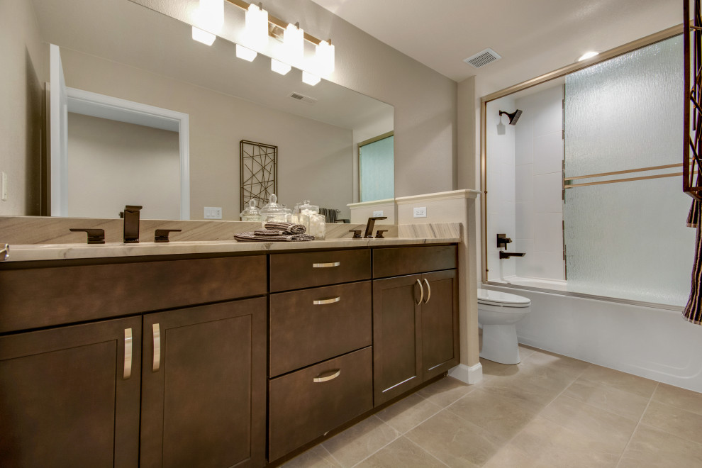 Пример оригинального дизайна: ванная комната среднего размера в стиле кантри с фасадами с утопленной филенкой, коричневыми фасадами, ванной в нише, душем над ванной, раздельным унитазом, серой плиткой, мраморной плиткой, серыми стенами, полом из керамогранита, врезной раковиной, мраморной столешницей, коричневым полом, душем с раздвижными дверями и серой столешницей