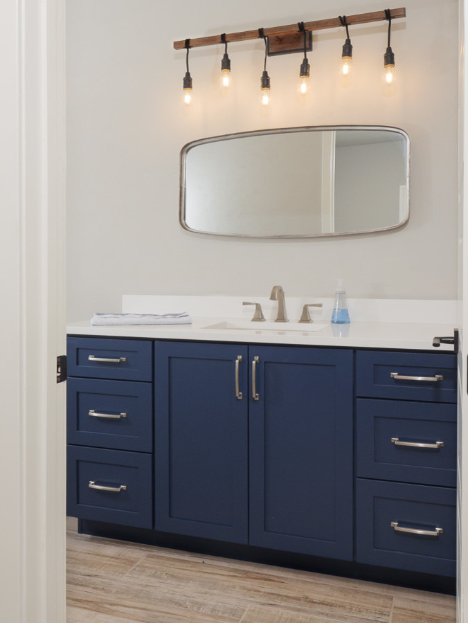 Photo of a large country family bathroom in Jacksonville with shaker cabinets, blue cabinets, an alcove bath, a shower/bath combination, a two-piece toilet, white tiles, metro tiles, grey walls, porcelain flooring, a submerged sink, engineered stone worktops, white floors, an open shower and white worktops.