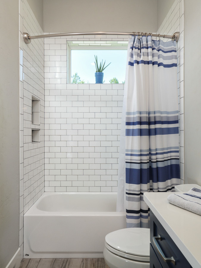 This is an example of a large rural family bathroom in Jacksonville with shaker cabinets, blue cabinets, an alcove bath, a shower/bath combination, a two-piece toilet, white tiles, metro tiles, grey walls, porcelain flooring, a submerged sink, engineered stone worktops, white floors, an open shower and white worktops.