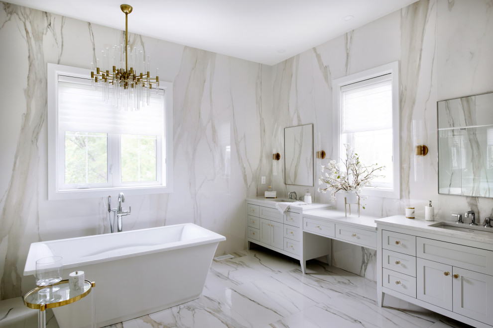 На фото: большая главная ванная комната в стиле неоклассика (современная классика) с отдельно стоящей ванной, белой плиткой, белыми стенами, белым полом, белой столешницей, серыми фасадами, мраморной плиткой, мраморным полом, врезной раковиной, окном и фасадами в стиле шейкер